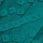 A collection of scrabble tiles on a wood table. A series of the letters spell "Mindfulness".